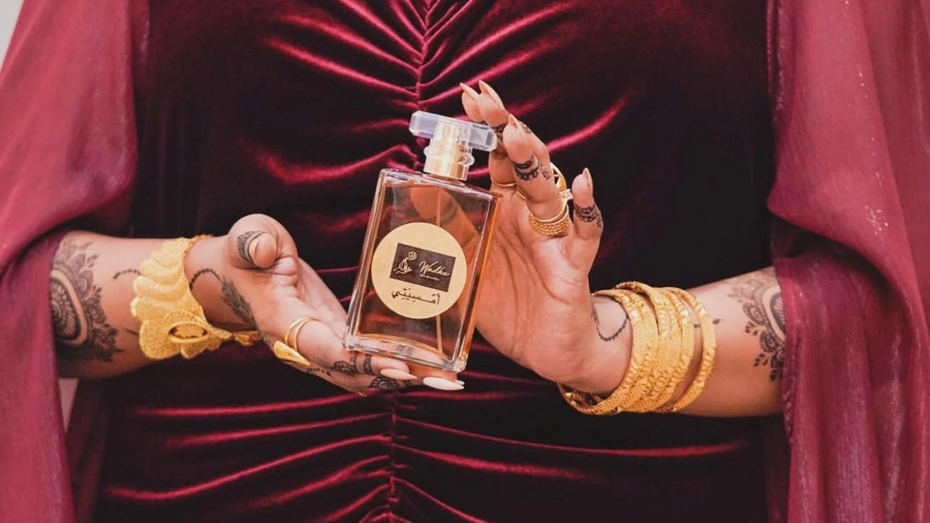 Woman in a red velvet outfit holding a perfume bottle with a blurred background